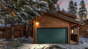 A wooden cabin with a green garage door, surrounded by snow-covered trees. - Golf Course views, Deer in yard, Next to Lake (McCall)