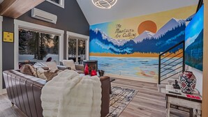A cozy living room with a large window, a fireplace, and a mural of mountains. - Golf Course views, Deer in yard, Next to Lake (McCall)