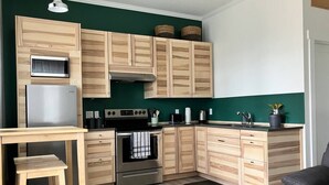 A modern kitchen with wooden cabinets, a stainless steel refrigerator, a built-in oven, and a black countertop. - Birch Suite Hillside (Golden)