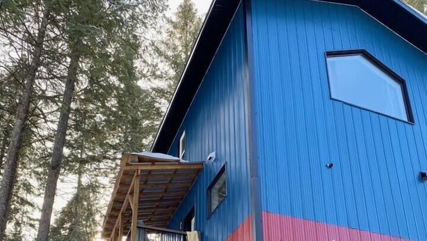 A multi-story building with a blue and red exterior, a wooden balcony, and a snow-covered ground. - Birch Suite Hillside (Golden)