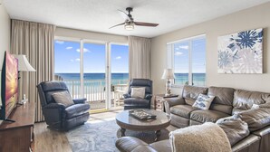 A spacious living room with a leather sofa, a recliner, and a coffee table. A ceiling fan is visible, and the room has large windows with a view of the ocean. - Majestic Sun B314*GulfViews*Owner's Garage*Hot Tub*Heated Pools*Beach Gears*Gym (Miramar Beach)