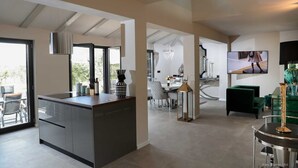 Eine moderne Küche mit Kochinsel, ein Essbereich mit einer Pendelleuchte und ein Wohnzimmer mit Fernseher und grünem Sofa.