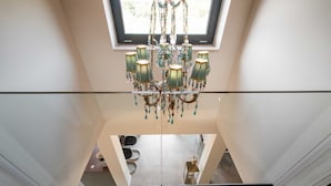 Ein modernes Interieur mit Glasdecke, einem Chandelier und Blick auf einen darunterliegenden Essbereich.