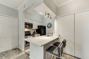 A modern kitchen with white cabinetry, a black refrigerator, and a stainless steel range hood.