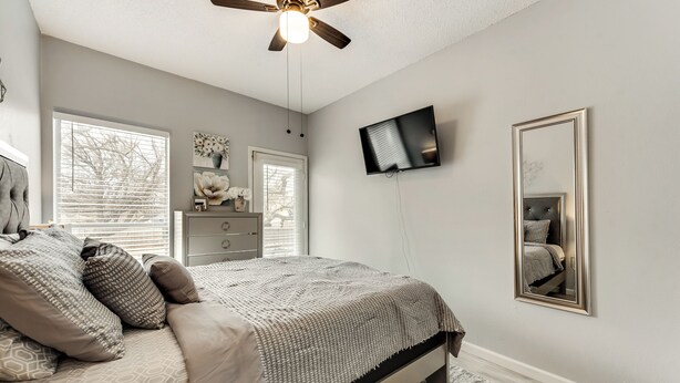 A bedroom with a bed, dresser, TV, and a ceiling fan.