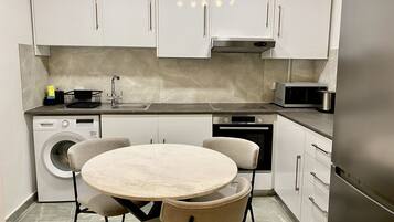 A compact kitchen with white cabinets, a built-in washing machine, a microwave, and a stainless steel refrigerator.