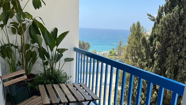 Un balcón con mesa y sillas de madera, plantas en macetas y vistas al mar.