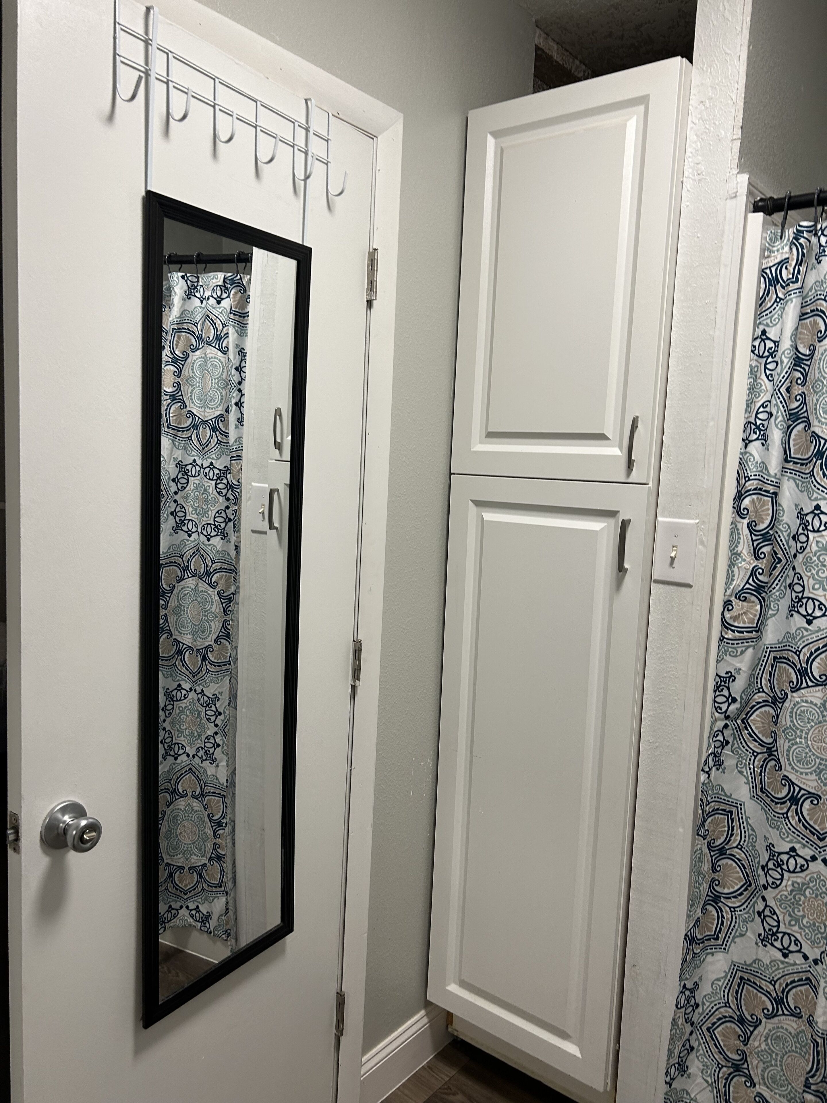 Une porte blanche avec un miroir, un rideau à motifs et une armoire blanche.