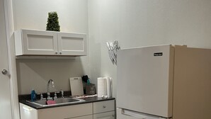 Une cuisine avec des meubles blancs, un réfrigérateur blanc, un évier et un plan de travail sur lequel se trouvent divers objets.