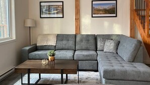 Una sala de estar con un sofá seccional gris, una mesa de centro de madera y dos cuadros en la pared.