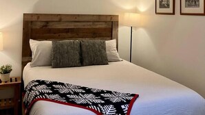 Un dormitorio con cabecera de madera, cama con ropa de cama blanca, una lámpara de noche y dos cuadros en la pared.