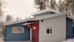 Una cabaña moderna con techo inclinado, puerta roja y una ventana.