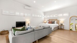 A modern bedroom with a large bed, a sofa, a TV, and a mirror.