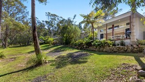 A house with a stone retaining wall, a covered porch, and a grassy yard with trees.