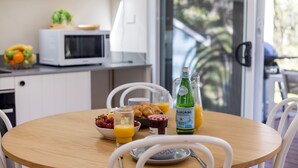 A breakfast table with croissants, fruit, and beverages, a microwave, and a view of the outdoors.