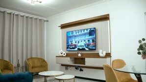 A modern living room with a flat-screen TV mounted on the wall, two armchairs, a small coffee table, and a glass-top table. - Medon Luxury Suites with power back up (Sandton)