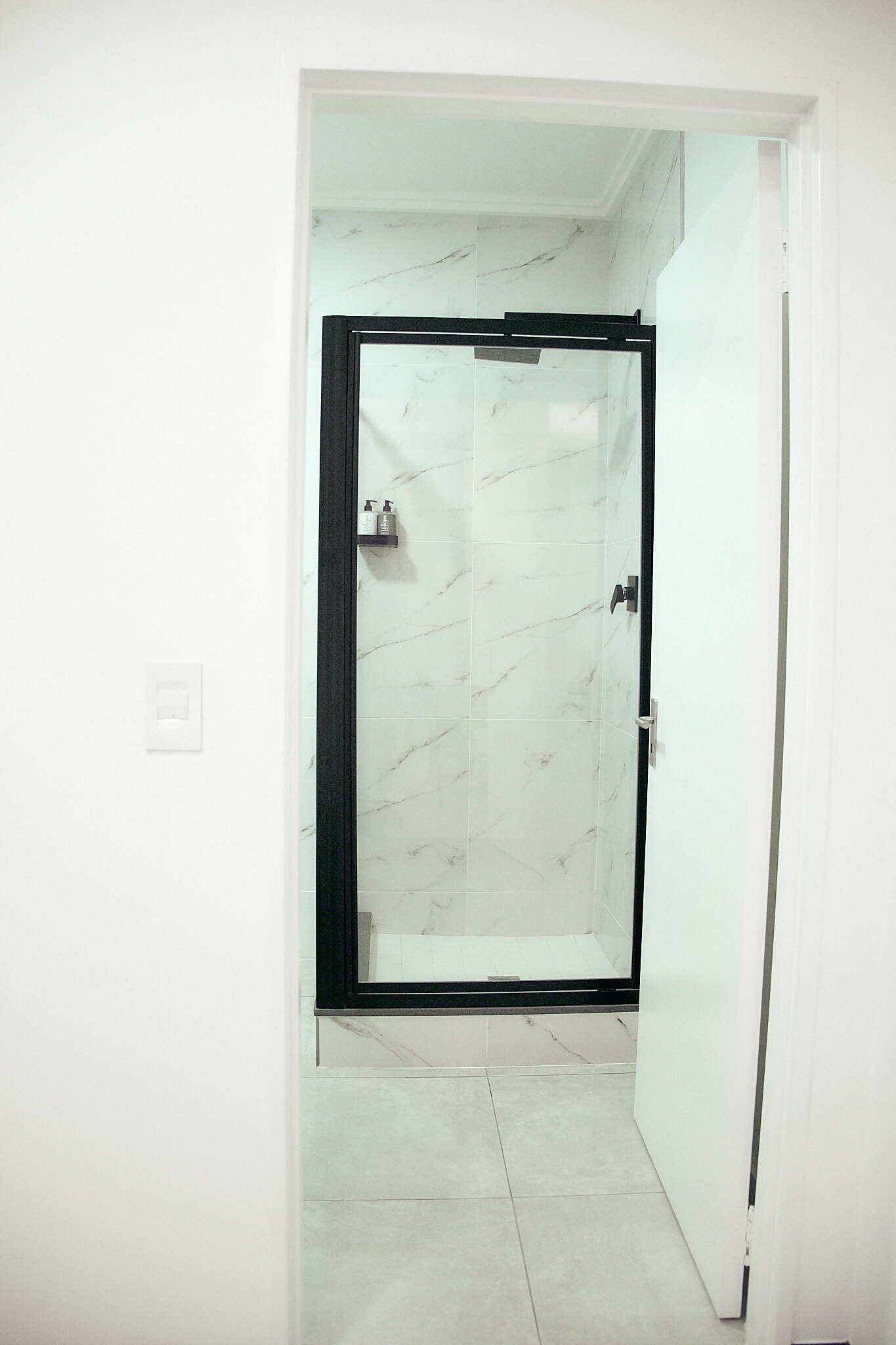Un bagno con doccia in vetro, pareti piastrellate di bianco e pavimento bianco.
