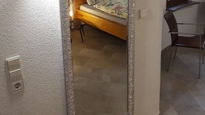 A room with a large mirror, a bed with floral bedding, a chair, and a small table.