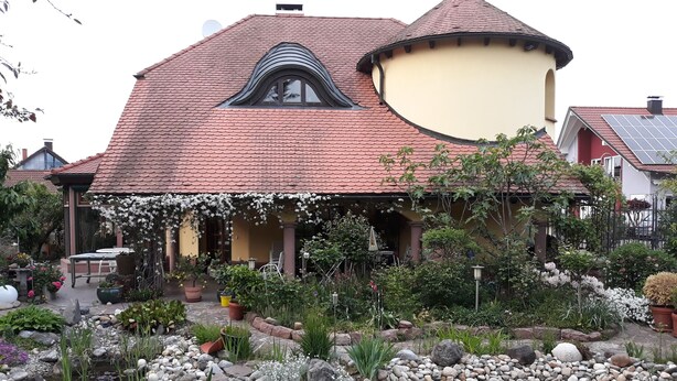 A house with a curved roof, a garden with a pond, and a solar panel on the roof.