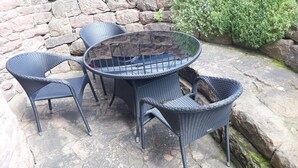 A set of four wicker chairs and a round table with a stone wall backdrop.