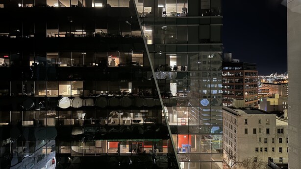 Un edificio moderno con varios pisos, ventanas amplias y fachada de vidrio que refleja el paisaje urbano.