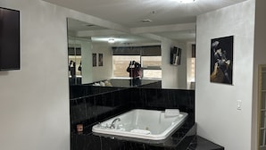 Un baño moderno con un espejo grande, encimeras de mármol negro, una bañera blanca y una alfombra con motivos dorados.