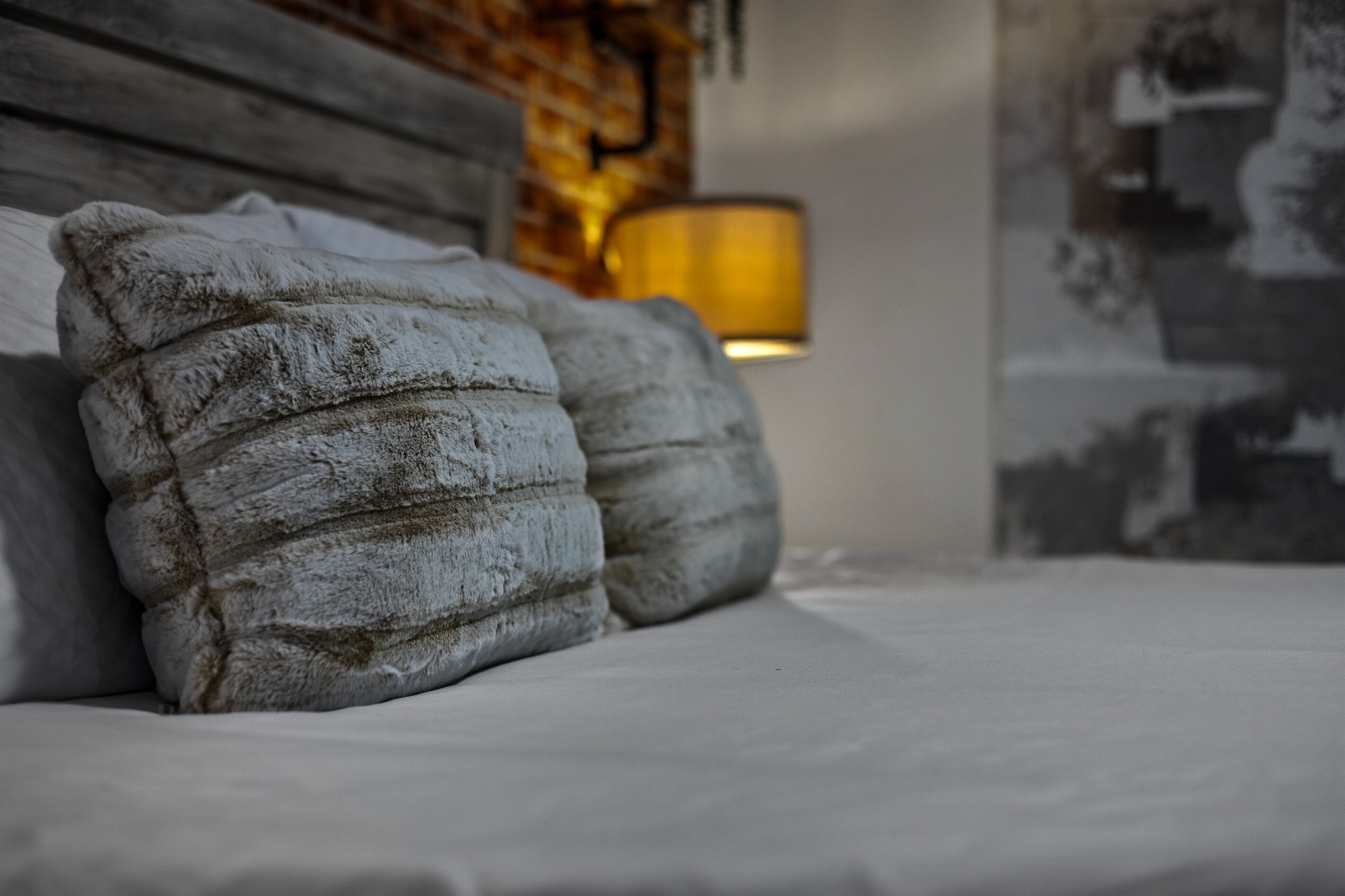 Una cama con almohadas mullidas y una lámpara fijada a la pared.
