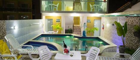 Un hotel con piscina, sillas de descanso y barandilla de vidrio.