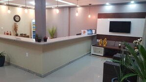 A reception area with a counter, potted plants, a clock, a television, and a seating area with cushions. - Pousada Maragolfinho (Maragogi)