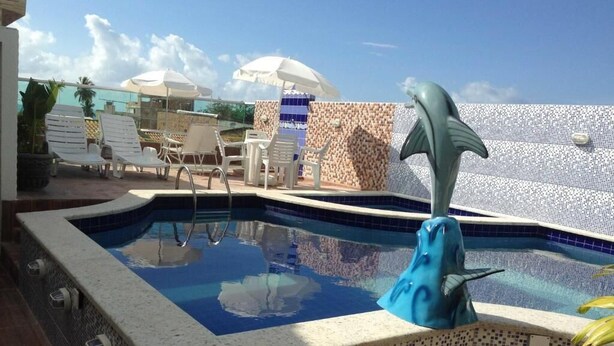A swimming pool with a dolphin statue, lounge chairs, and umbrellas. - Pousada Maragolfinho (Maragogi)