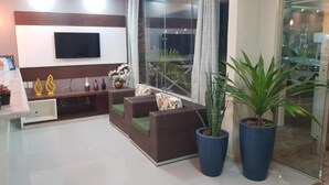 A modern living room with a flat-screen TV, wicker furniture, and large potted plants. - Pousada Maragolfinho (Maragogi)