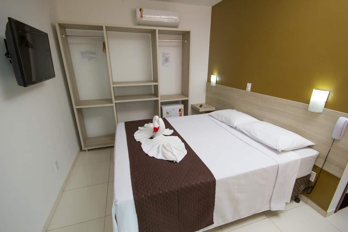 Une chambre d’hôtel équipée d’un lit, d’une armoire, d’une table de chevet, d’un téléphone et d’un appareil de climatisation.