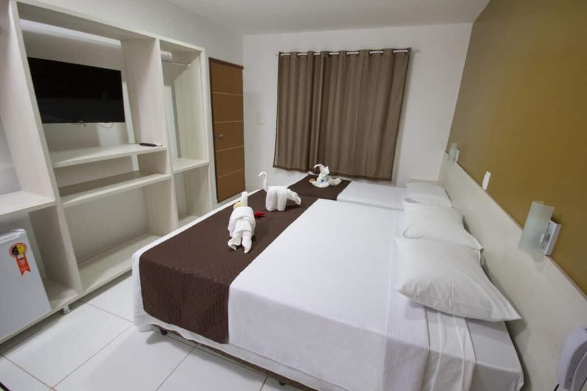 Une chambre d’hôtel avec deux lits, une télévision, une armoire et un petit réfrigérateur.
