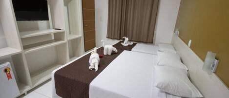 Habitación de hotel con dos camas, televisión, armario y un refrigerador pequeño.