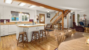 A spacious kitchen with wooden flooring, a large island with stools, and a staircase leading to a loft area. - Somers Lookout on Flathead Lake, private dock (Somers)