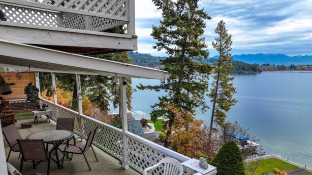 A covered outdoor patio with a table and chairs, overlooking a lake with trees and mountains in the background. - Somers Lookout on Flathead Lake, private dock (Somers)