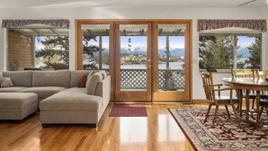 A living room with a sectional sofa, a dining table with chairs, and a view of mountains through glass doors. - Somers Lookout on Flathead Lake, private dock (Somers)
