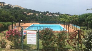 Piscina rodeada por una zona vallada con un cartel, con colinas y vegetación al fondo.