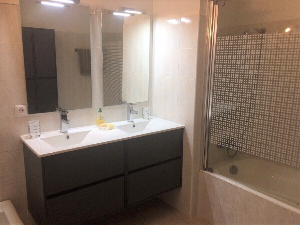 Ein Badezimmer mit Doppelwaschbecken, dunklem Schminktisch, Spiegel und einer Dusche mit Glastür.