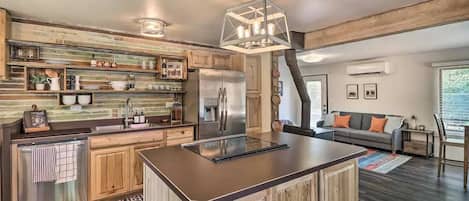 Una cocina moderna con armarios de madera, una isla central, electrodomésticos de acero inoxidable y una lámpara colgante.