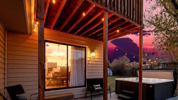 En overdækket terrasse med et spabad, udendørs møbler og en skydedør til et indre rum.