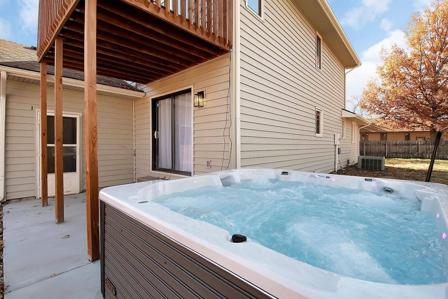 Un jacuzzi dans un jardin, avec une terrasse en bois et une maison en arrière-plan.