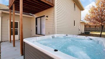 Un jacuzzi dans un jardin, avec une terrasse en bois et une maison en arrière-plan.