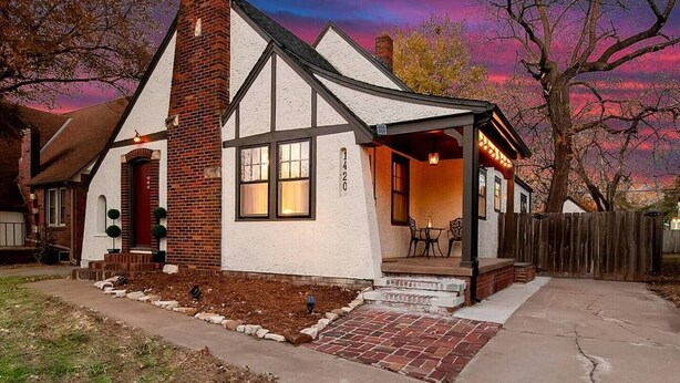 A two-story house with a chimney, a porch with outdoor seating, and a brick driveway. - Riverside Renaissance - Spa!  King Beds! Beautiful Renaissance decor (Wichita)