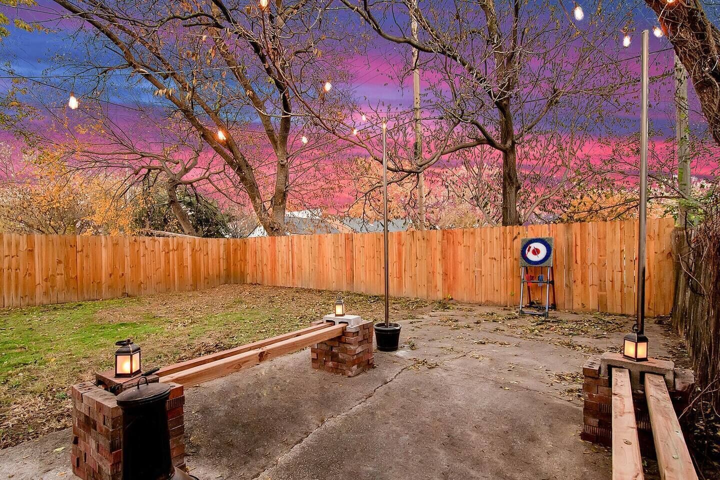 A backyard with a wooden fence, a seesaw, and lanterns.