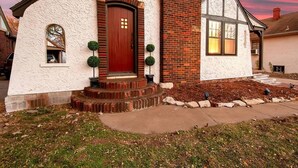 A two-story house with a red door, brick chimney, and a small porch with potted plants. - Riverside Renaissance - Spa!  King Beds! Beautiful Renaissance decor (Wichita)