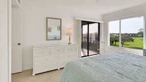 Un dormitorio con cama, cómoda, lámpara, espejo y balcón con vistas al exterior.