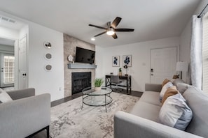 A living room with a fireplace, a ceiling fan, a TV, and a dining area with a table and chairs.