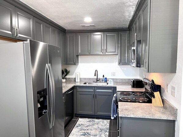 A kitchen with grey cabinets, a stainless steel refrigerator, a sink, a stove, and a countertop with a knife block.