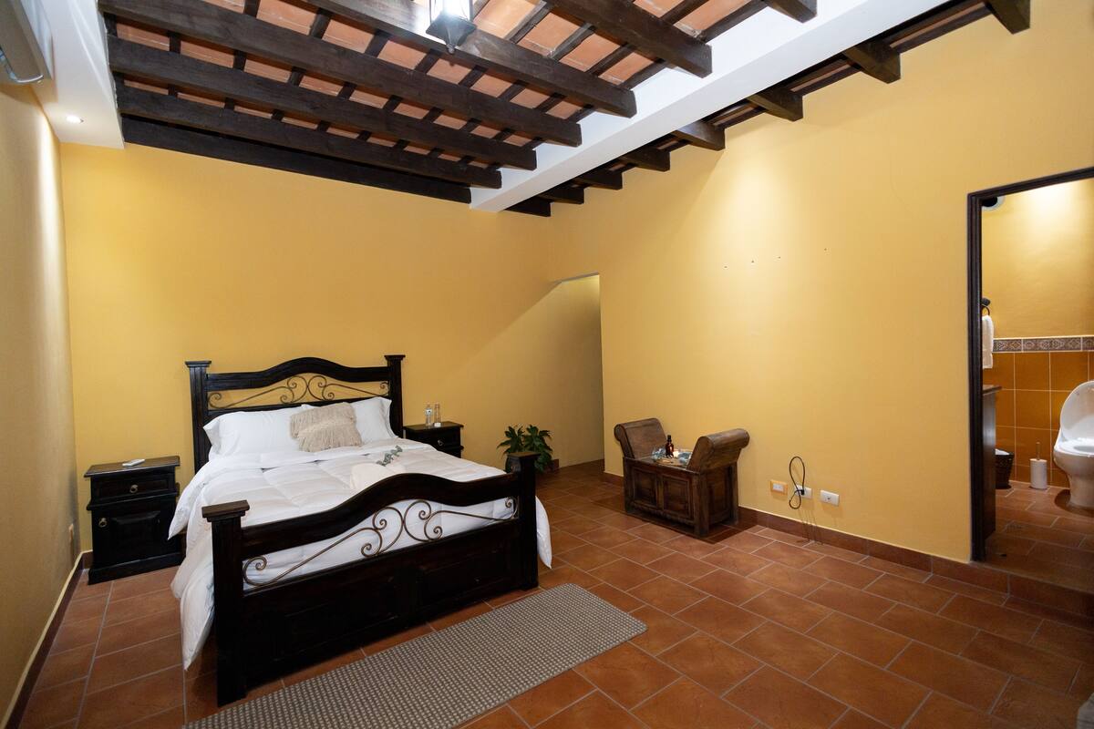 Une chambre à coucher avec un lit, des tables de chevet, une chaise, une petite table et une plante en pot.